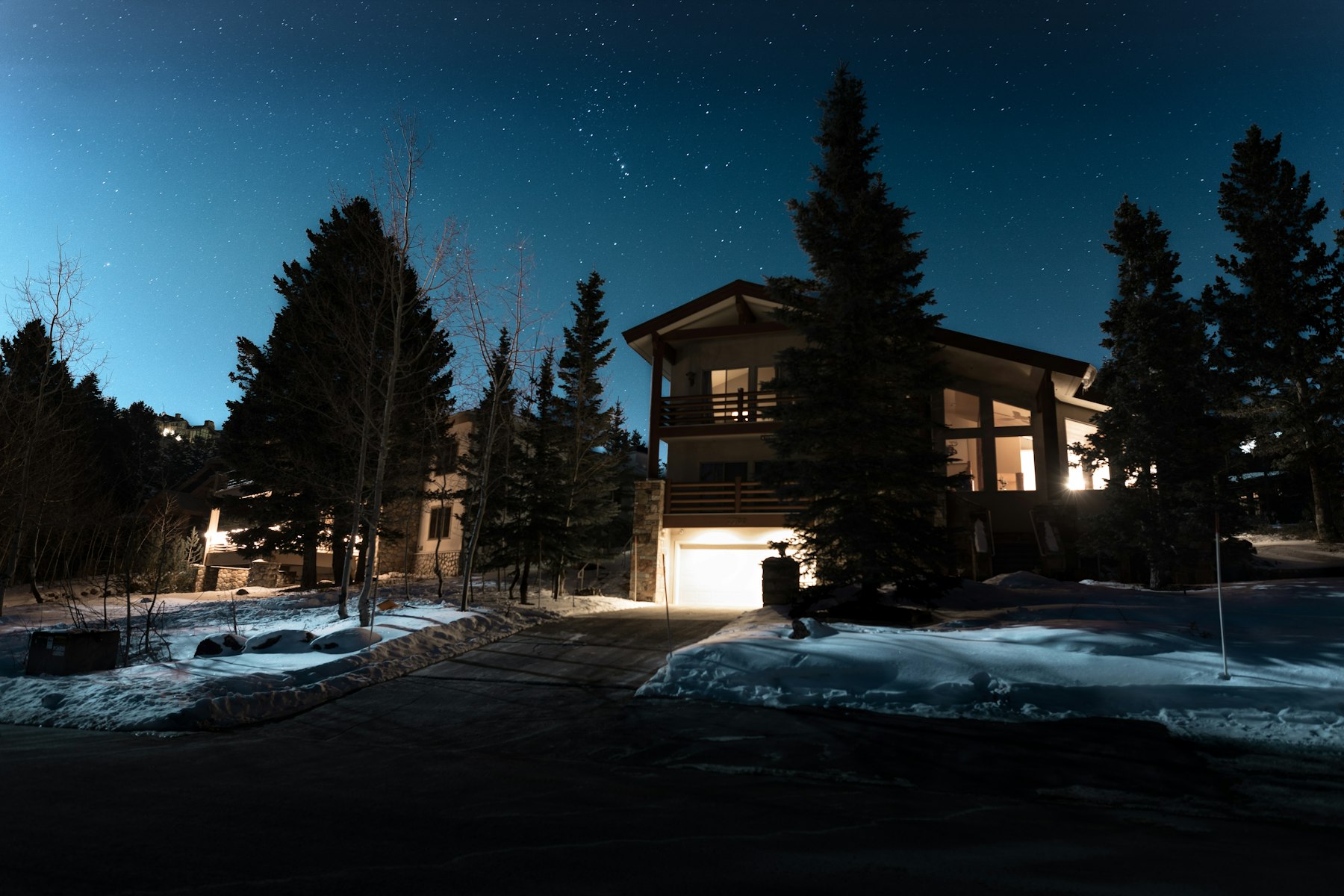 The Holland house at dusk among pines, windows lit warm over snow.