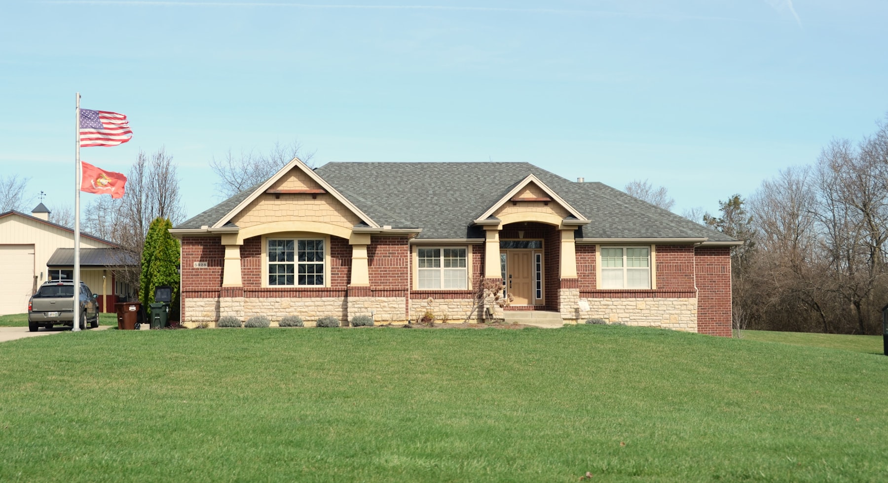A brick ranch house with a wide green lawn under a sunny sky.