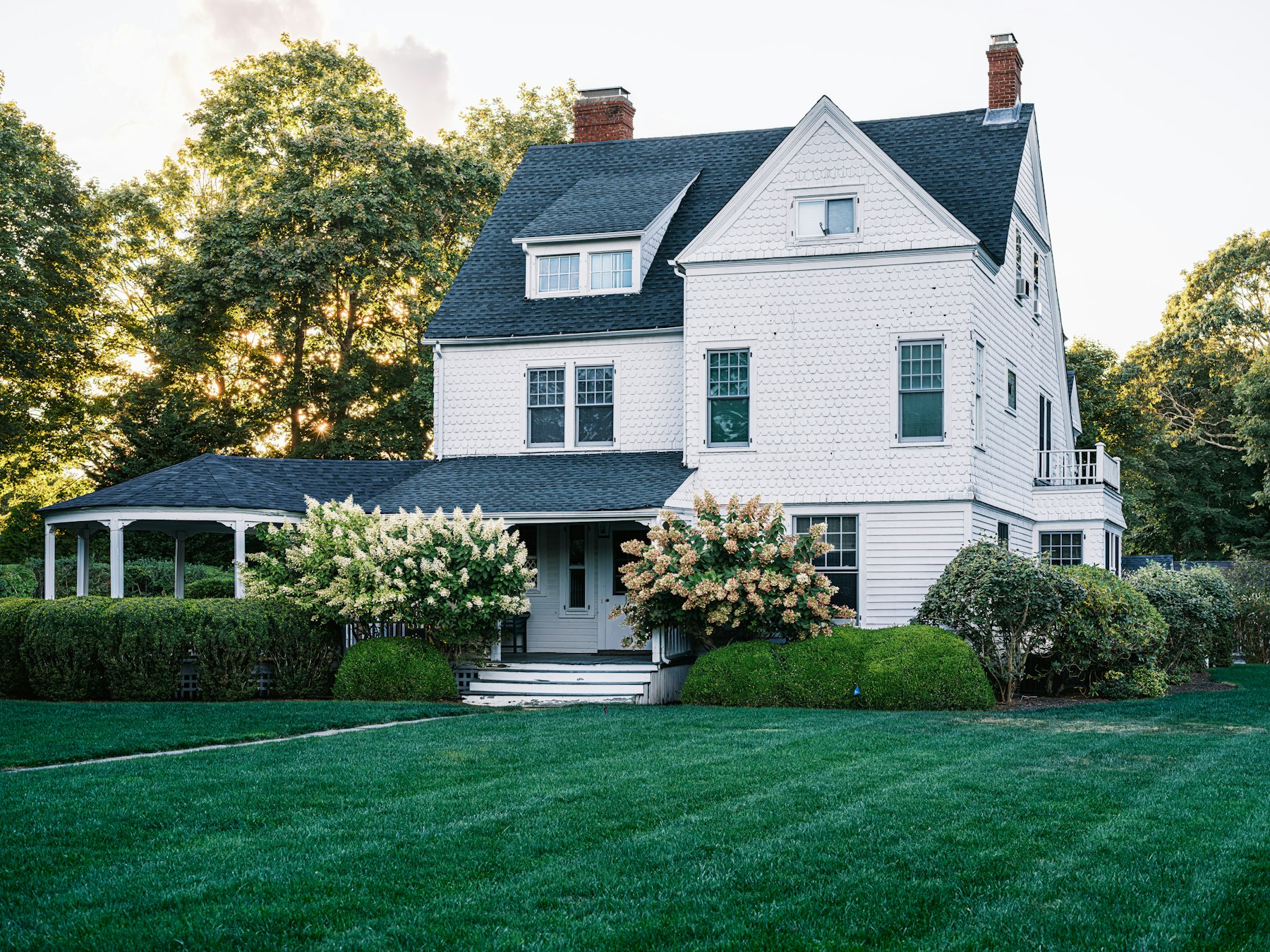 A large white house with a wide lawn and mature trees.