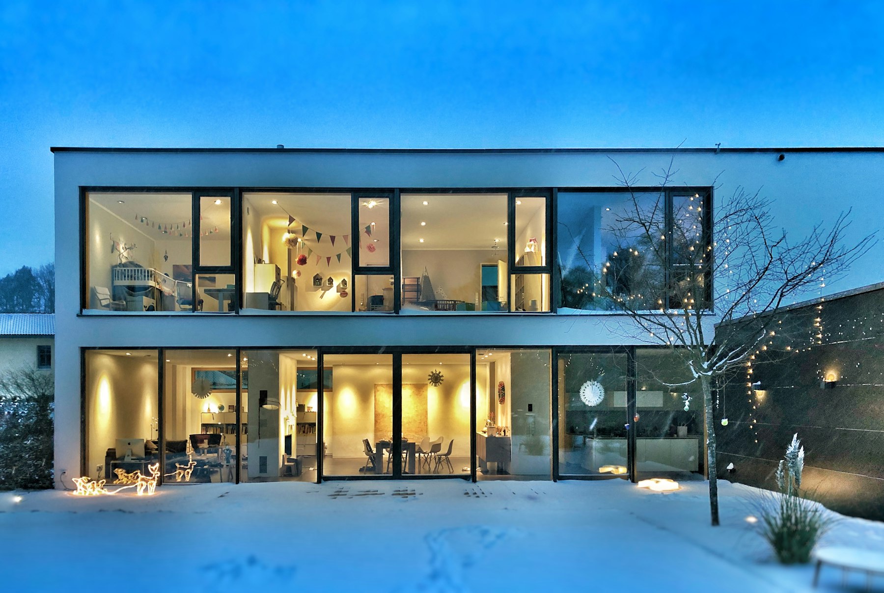 A Beckenbauer house at blue hour: every window lit warm against snow and a deep blue sky.